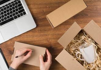 Laptop obok otwartego kartonowego pudełka z wypełniaczem i ceramicznym kubkiem, symbolizujący obowiązki BDO dla sklepów internetowych w zakresie opakowań.