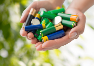 Zbliżenie na dłonie trzymające kolorowe baterie. Grafika promuje ofertę EKOKONSULT dotyczącą obowiązków środowiskowych związanych z bateriami.