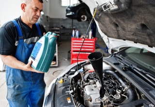 Mechanik w warsztacie samochodowym trzymający kanister z olejem nad otwartą maską samochodu, w którym umieszczono lejek. Zdjęcie ilustruje proces powstawania oleju odpadowego w warsztacie lub serwisie OZE, gotowy do ewidencji w BDO z pomocą EKOKONSULT.